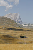 Blick auf goldene Wiesen, die sich unter einem heiteren Himmel in Richtung des majestätischen Gran Sasso-Gebirges erstrecken, eine ruhige Szene in Isola del Gran Sasso D'italia, Abruzzen, Italien.