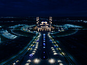 Aerial view of the illuminated Hazrat Sultan Mosque standing majestically under the night sky, its golden lights contrasting against the dark surroundings, Astana, Astana, Kazakhstan.