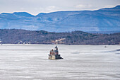 Aerial view of the iconic Hudson-Athens Lighthouse standing resilient amidst the cold waters, with a backdrop of hazy mountains and serene skies, Hudson, New York, United States.