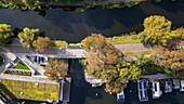 Aerial view of the vibrant Brda River flowing under a quaint bridge, flanked by autumnal trees and houseboats, Bydgoszcz, Województwo kujawsko-pomorskie, Poland.