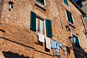 View of brick buildings with vibrant green shutters and laundry hanging from a window, creating a charming scene, Siena, Tuscany, Italy.