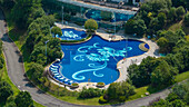 Aerial view of a uniquely shaped, blue swimming pool adorned with ornate floral patterns, nestled amidst verdant trees and winding pathways, Zhangjiajie, Hunan, China.