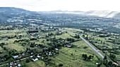 Aerial view of a highway cutting through verdant fields and scattered homesteads, with distant hills adding depth to the landscape, Eldoret, Kenya.