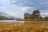 View of ancient stone castle standing resiliently against the backdrop of moody skies and tranquil waters, its reflection shimmering, Dornie, Scotland.