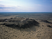 Aerial view of the ancient fortress ruins standing proud against the vast desert plain under a hazy sky, Ayaz Kala, Republic of Karakalpakstan, Uzbekistan.