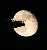 View of a colossal moon looming behind a silhouetted observation deck filled with tiny figures gazing at the celestial spectacle, New York, New York, United States.