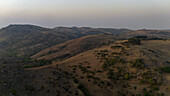 Aerial view of undulating hills under a pale sky, the sun-kissed terrain casting long shadows in the serene landscape, Njawai, Taraba, Nigeria.