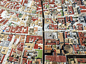 Aerial view of a vibrant tapestry of red-tiled rooftops and sun-bleached walls meet in a geometric dance of urban architecture, Cádiz, Andalusia, Spain.