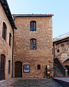 View of aged stone buildings standing tall in the town square, their windows like eyes gazing out over the ancient cobblestones, San Gimignano, Tuscany, Italy.