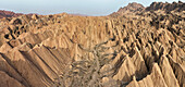 Aerial view of the parched, rugged landscape of the Tianshan Mountains, with its sharp peaks and deep valleys, bathed in the warm light of the setting sun, Ürümqi, Xinjiang, China.