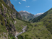 Aerial view of a serpentine river threading through a vibrant green valley embraced by rugged, rocky mountains under a clear blue sky, Sethan, Himachal Pradesh, India.