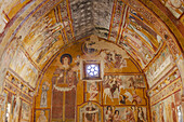 View of vibrant frescoes dance across the arched ceiling, depicting biblical scenes in rich ochre and crimson hues, Bominaco, Abruzzo, Italy.
