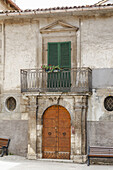 View of an old building with a bright orange door and striking green shutters from a ground perspective, Scanno, Abruzzo, Italy.