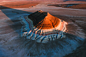 Aerial view of a majestic mountain bathed in the warm glow of the setting sun, casting long shadows across the arid landscape, Mount Bokty, Mangystau Region, Kazakhstan.