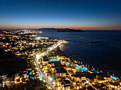 Aerial view of the coastline lit up with a warm glow contrasting the deep blue of the sea and sky, Crete, Greece.