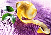 Zitrone mit dünn abgeschnittener Schale auf lila Untergrund