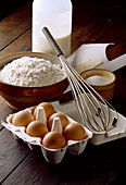 Zutaten für Crêpes auf Holzuntergrund: Eier, Milch, Mehl, Butter mit Schneebesen