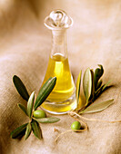 Eine Karaffe mit Olivenöl und frischen Oliven auf grobem Tuch