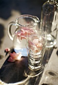 Karaffe mit Wasser und Rosenblütenblättern, dazu Gläser