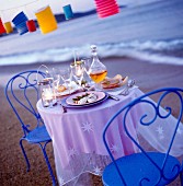 Gedeckter Tisch am Strand mit Speisen, Getränken, Kerzen und Lampions für Zwei