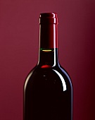 Flasche Rotwein vor rotem Hintergrund (Ausschnitt)