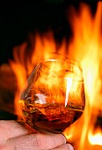 Hand hält einen Schwenker Cognac vor offenem Kamin