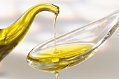 Von einem Kännchen Olivenöl auf einen Löffel gießen