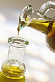 Von einem Kännchen Olivenöl in eine Glasflasche gießen