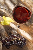 Glas mit Rotwein und rote Trauben auf Holzuntergrund