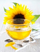 Sonnenblumenöl in einem Schälchen mit Sonnenblumenkernen und Sonnenblume