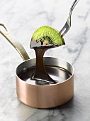 Dipping a slice of kiwi into a saucepan of melted chocolate