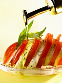 Pouring olive oil onto a dish of tomatoes and mozzarella