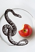 Schlange und angebissener Apfel auf Glasteller