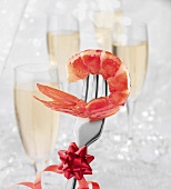 Shrimp auf einer Gabel, Champagner in Gläsern im Hintergrund