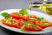 Pouring olive oil onto a tomato and basil salad