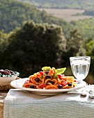 Plate of noodles with tomatoes and olives on a table outdoors