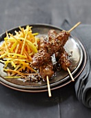 Yakitori chicken brochettes caramelized with sesame seeds,thinly sliced yellow and orange carrots