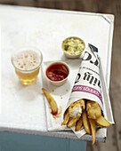 Fish and Chips in Zeitungspapier gewickelt mit Dips und einem Glas Bier