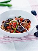 Sautéed pork with baked plums and red and green peppers