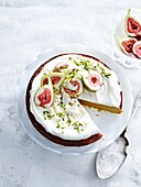 Overhead view of orange and almond cake with yoghurt cream, pistachios, figs and cake server