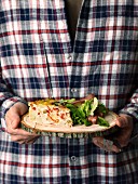 Person holding a slice of Spanish tortilla on a round wooden board
