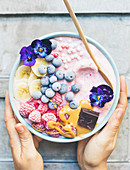 Hands carrying a raspberry,blueberry,toffee,pansy and square of chocolate smoothie bowl
