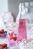 Glass of berry cordial with fresh fruit, bottle of cordial beside glass, close-up