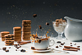Cane sugar cubes splashing in cup with hot black coffee in front of biscuits and spices
