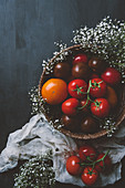 Fresh red tomatoes in wicker bowl with white flowers on wooden background