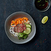 A slice of roast beef on vegetable noodles and cucumber slices