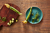 Frische Zucchini mit Blütenansatz auf Teller und Holzbrett