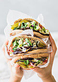 Hände halten drei Pita-Sandwiches mit Falafel und Gemüse