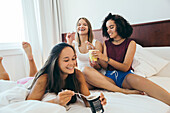 Three female teenagers laughing and eating ice cream on a bed
