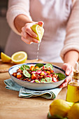 Woman squeezing lemon on a quinoa salad with radish and squash